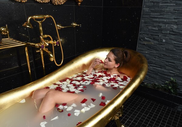 Frau in goldener Badewanne mit Rosenblüten